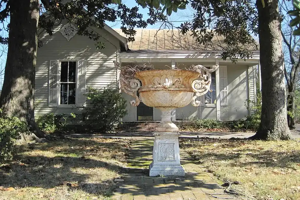 Historic cottage with an ornate garden urn on a brick path under magnolia trees in Germantown, Tennessee